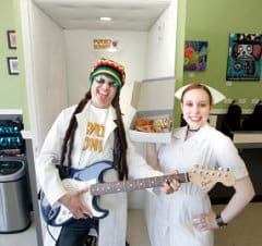 jazdylan Jordan Zweigoron, chief psycho, and Dylan Syrett, nurse, stand with guitar and donuts in front of the shop's new music studio, where customers can play the electric guitar. (George Sakkestad/Campbell Reporter)
