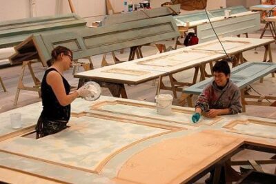 Erin Wilson and Christina Barretti-Sigal paint and distress a set wall in the scene shop at the Tony Award-winning Berkeley Repertory Theatre. Photographer: Lisa Lázár