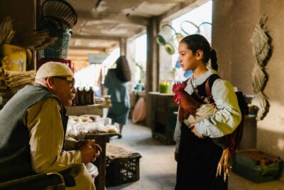Lamia, a schoolgirl holding a rooster, speaks with an elderly man in a busy Iraqi market in The President’s Cake.