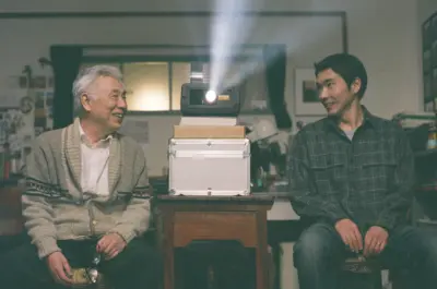 Issey Ogata and Tasuku Emoto sit on either side of a slide projector in a photo studio in a scene from Memorizu