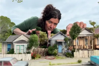 Filmmaker Anna Fitch leans over her miniature recreation of Yolanda Shea's Pacific Grove street in the documentary Yo (Love Is a Rebellious Bird)
