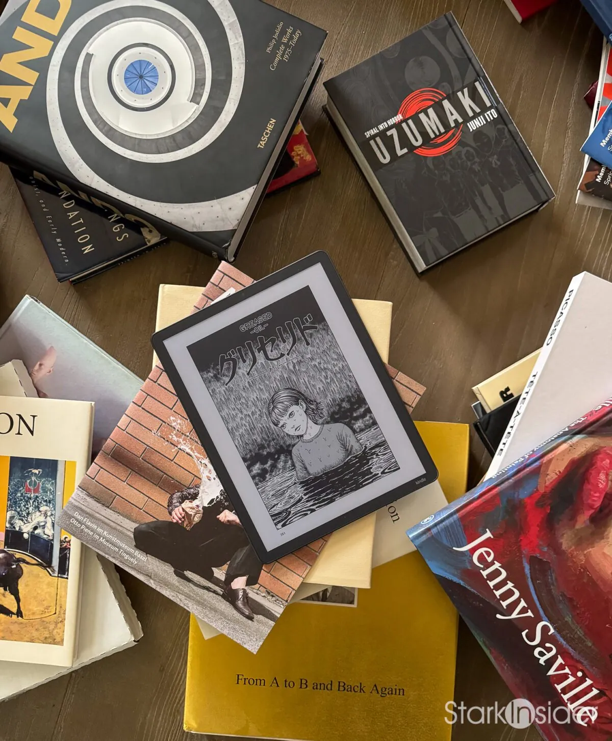 Overhead view of the Kindle Scribe Colorsoft showing a Junji Ito manga page, resting on a stack of art books including Tadao Ando, Uzumaki and Jenny Saville