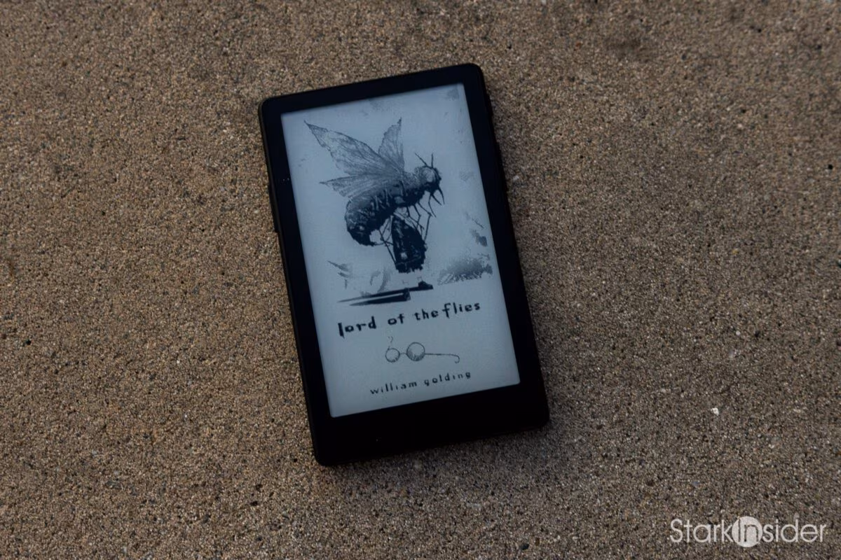 XTEINK X4 Pro pocket e-reader resting on sand, its e-ink sleep screen displaying the cover art for William Golding's Lord of the Flies