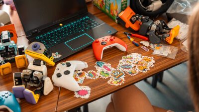 Several Microduck robots on a wooden table beside a laptop, game controllers and a spread of duck stickers